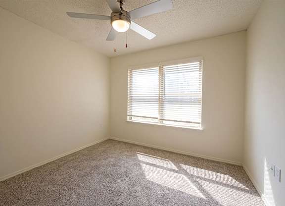 A room with a ceiling fan and a window with blinds.