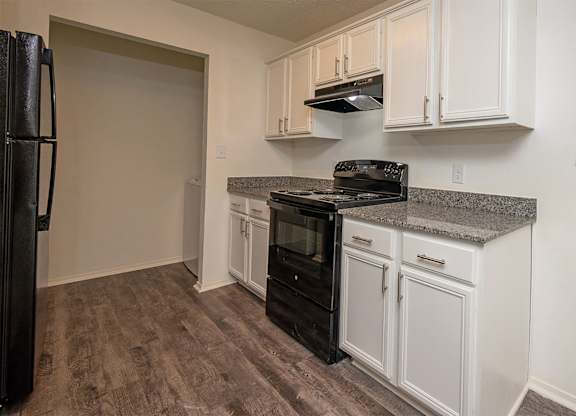 A kitchen with a black fridge, black stove, and white cabinets.