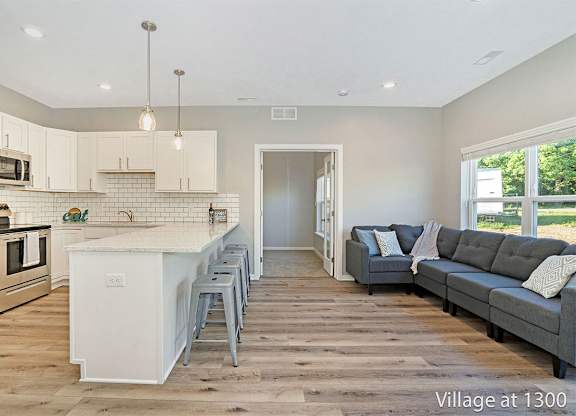 A kitchen with a white island and a grey couch in the living room.