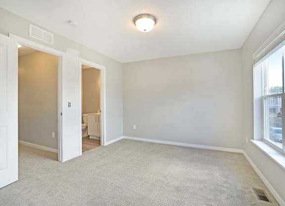 A spacious room with a carpeted floor and a window on the right side.