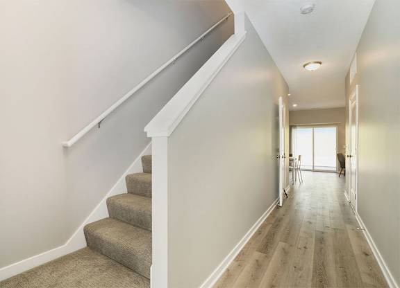 A hallway with a staircase and a person walking in the distance.