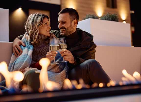 A couple is sitting close together, holding glasses of wine, and smiling at each other.