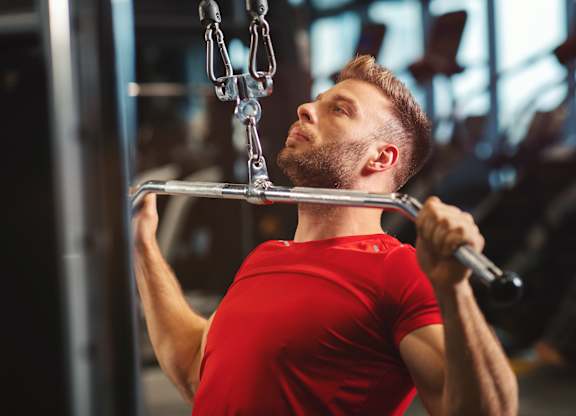 A man in a red shirt is working out on a pull-up bar in a gym.