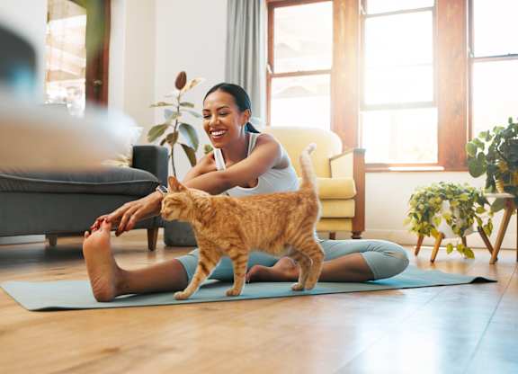 A woman is sitting on a yoga mat with her cat standing on it.