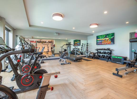 a gym with cardio machines and weights on a wooden floor