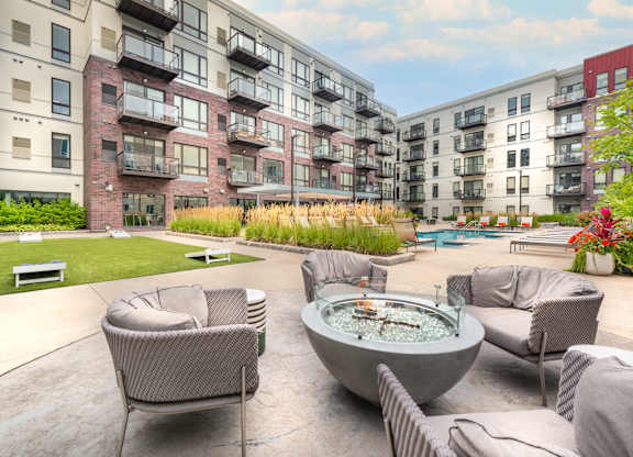 an outdoor patio with chairs and a fire pit in front of an apartment building