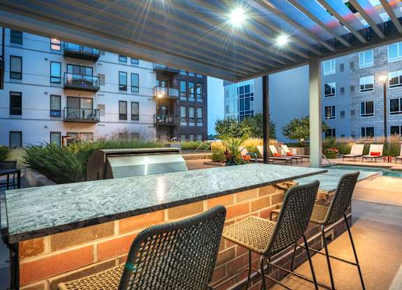 a patio with a bar and chairs in front of a pool