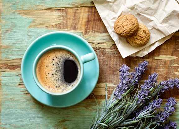 A cup of coffee with a biscuit and lavender on a wooden table.