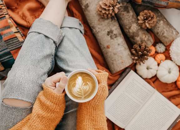 A person in a yellow sweater is holding a cup of coffee with a latte art design on it.