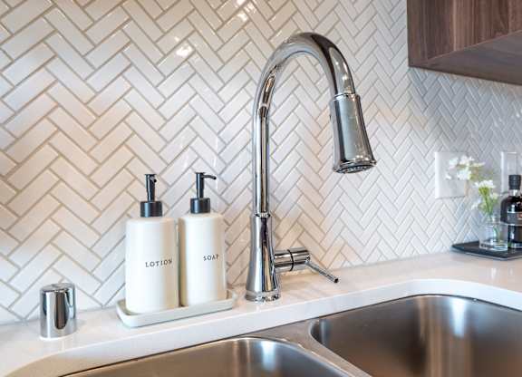 a kitchen sink with two bottles on the counter next to a faucet