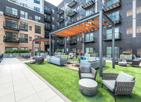 an outdoor lounge area with couches and tables in front of an apartment building