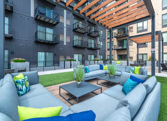 an outdoor lounge area with couches and tables in front of an apartment building