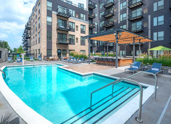 a swimming pool in front of an apartment building with a pool and chairs