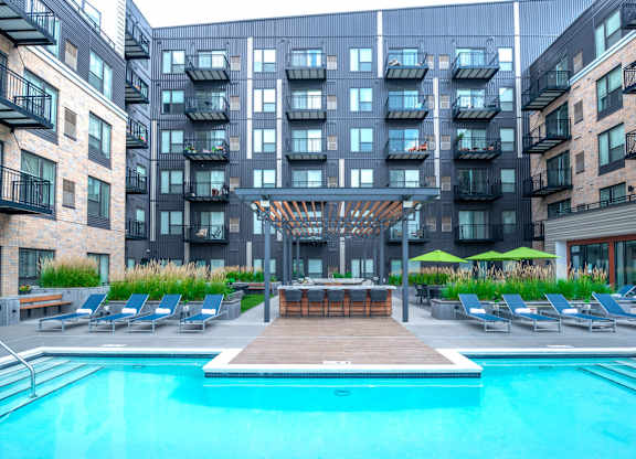 a swimming pool in front of an apartment building with a pool and lounge chairs