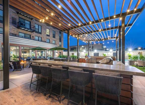 a patio with a bar and chairs at night