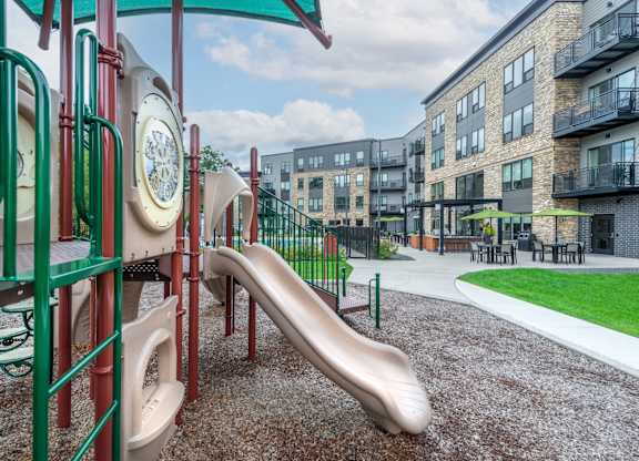 a playground with a slide and other playground equipment with apartments in the background