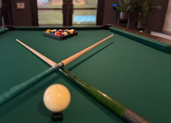 A pool table with a white ball in the middle and two cues crossed over it.