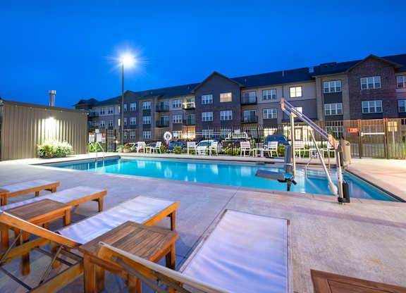 a swimming pool at night with picnic tables and an apartment building