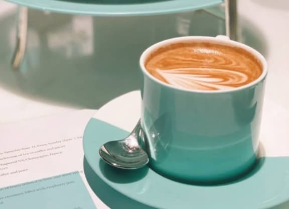 A cup of coffee with latte art and a piece of cake on a plate.