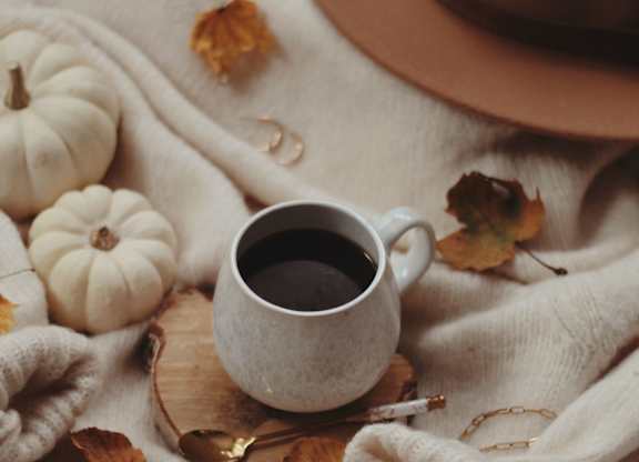 A cup of coffee surrounded by small white pumpkins and autumn leaves.