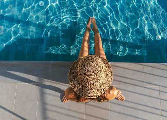 A woman in a straw hat is sitting on the edge of a pool.