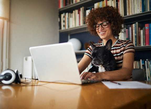 a woman sitting at a table with her dog using a laptop computer