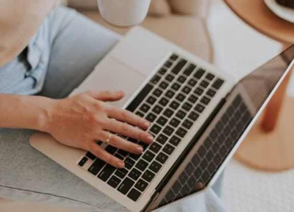 A person with curly hair is using a laptop and holding a cup of coffee.