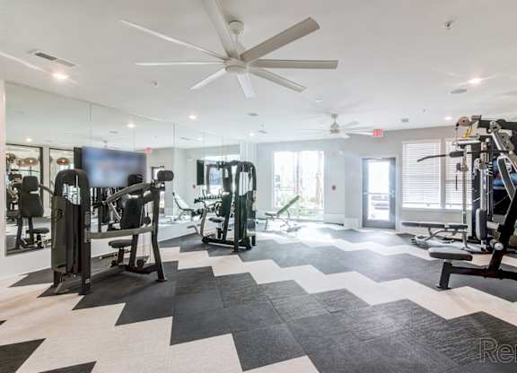 A spacious gym with a variety of equipment and a ceiling fan at Tapestry Nona Apartments in Orlando, FL