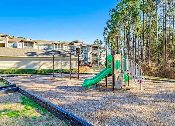 A playground with a green slide in front of a building.