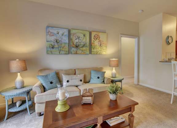 A living room with a white couch, a blue chair, a wooden coffee table, and a painting on the wall.