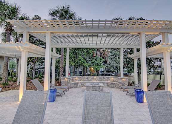 A white pergola with a stone fireplace underneath it.