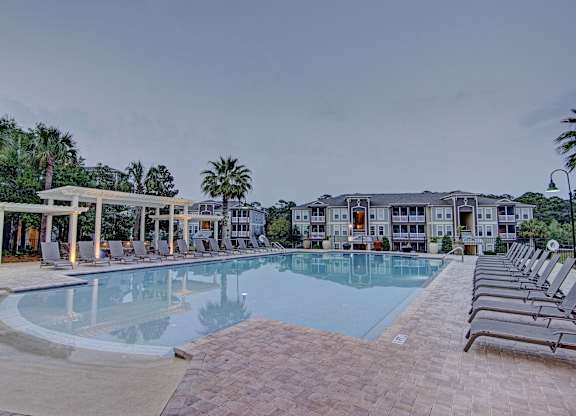 A large swimming pool surrounded by lounge chairs and a building in the background.