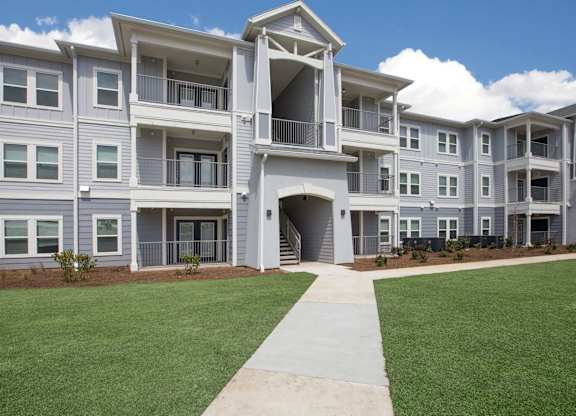 A large, modern apartment complex with a well-maintained lawn and clear skies.