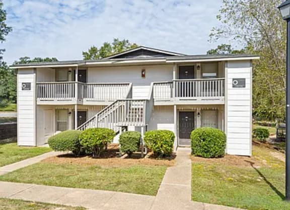 A white two-story apartment building with a balcony on the second floor.