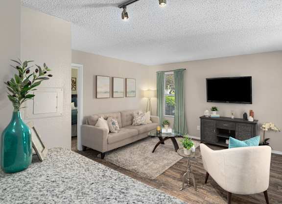 A living room with a grey sofa, a white armchair, a green vase, and a TV on the wall.