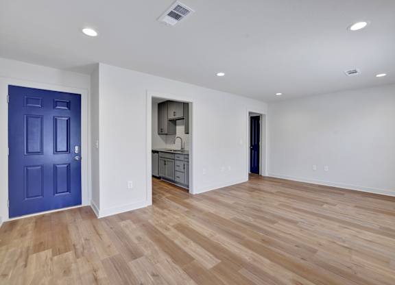 an empty living room with a blue door and a kitchen