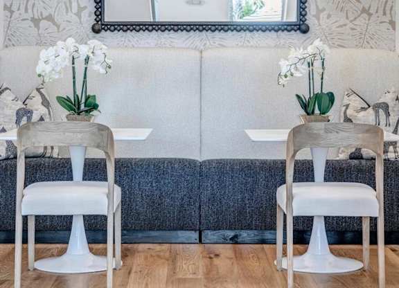 A dining room with a white table and chairs, a mirror, and a wallpapered wall.
