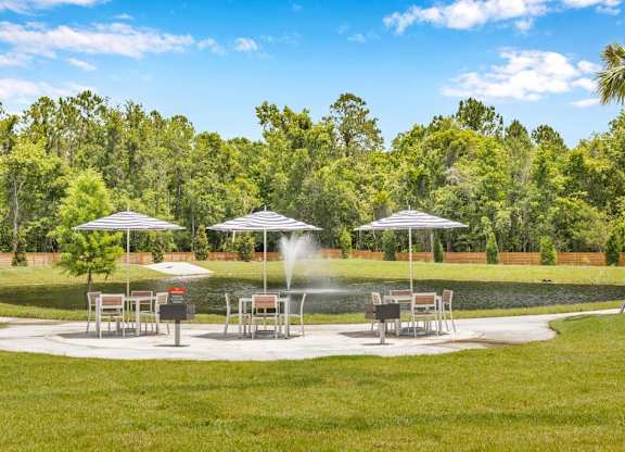 A park with a fountain and benches under umbrellas.