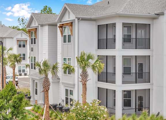 A row of white houses with balconies and palm trees in front.
