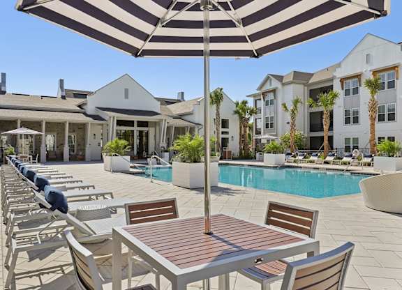 A striped umbrella shades a table and chairs by a pool.