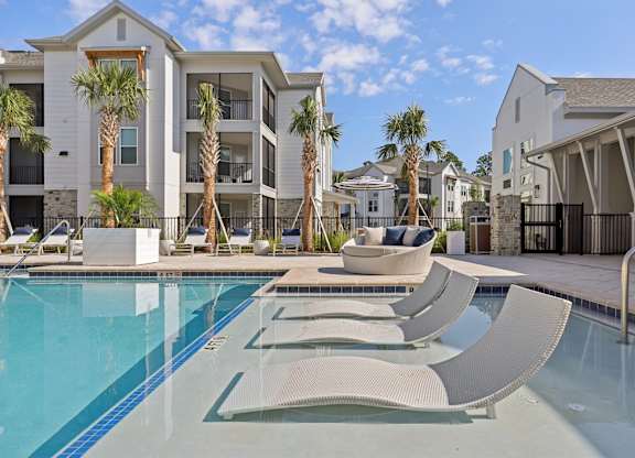 A pool with sun loungers and a building in the background.