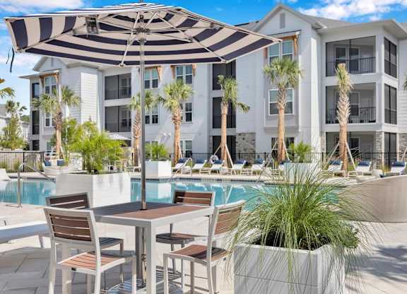 A patio with a table and chairs overlooking a pool.