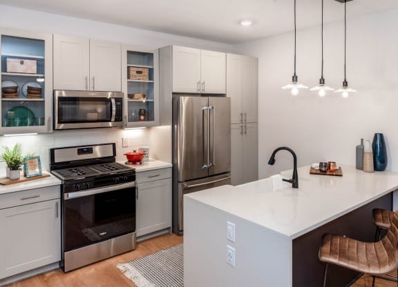 kitchen with waterfall quartz countertop island, pendant lighting, farmhouse sink, and glass cabinet fronts at Anthem Luxury Rentals and Apartments in Huntsville, AL