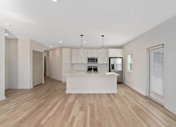 A spacious kitchen with wooden floors and white cabinetry.