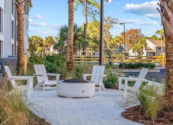 A white patio with a fire pit and chairs.