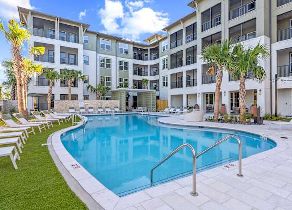 A swimming pool in front of a building with palm trees.