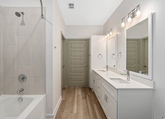 A bathroom with a white tub, sink, and a wooden floor.