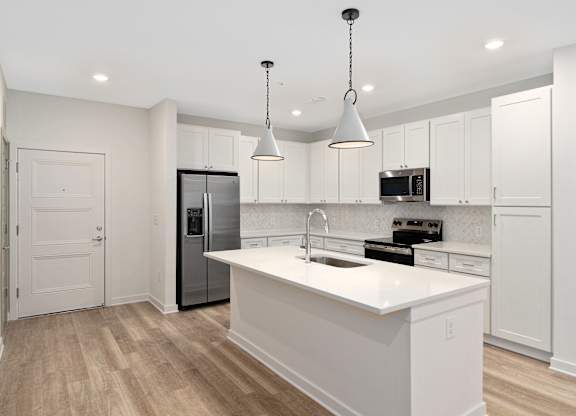 A modern kitchen with a white island and pendant lights.