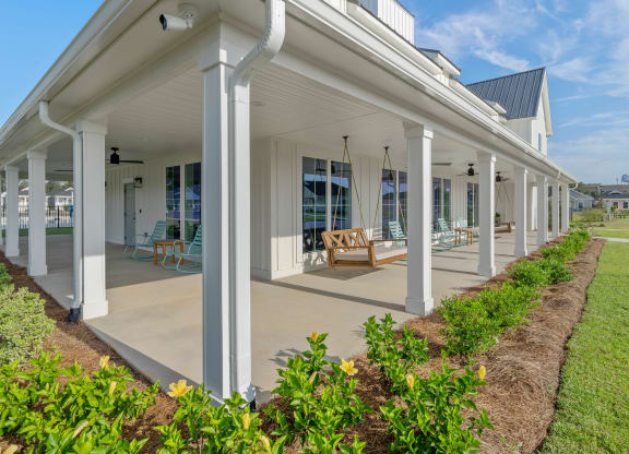 the front porch of a white house with columns and a porch swing at The Cottages at Foley Farms apartments in Foley, AL