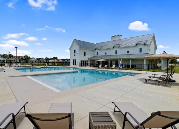 A large swimming pool with lounge chairs and a house in the background.